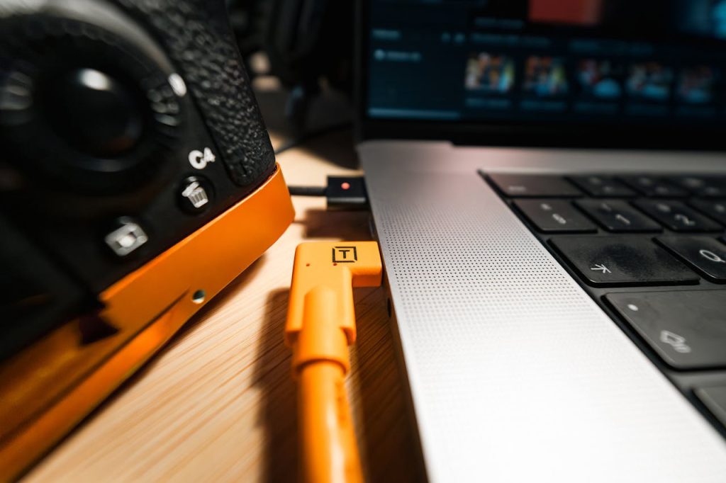 A close-up view of a camera connected to a laptop using an orange cable, highlighting studio equipment setup.