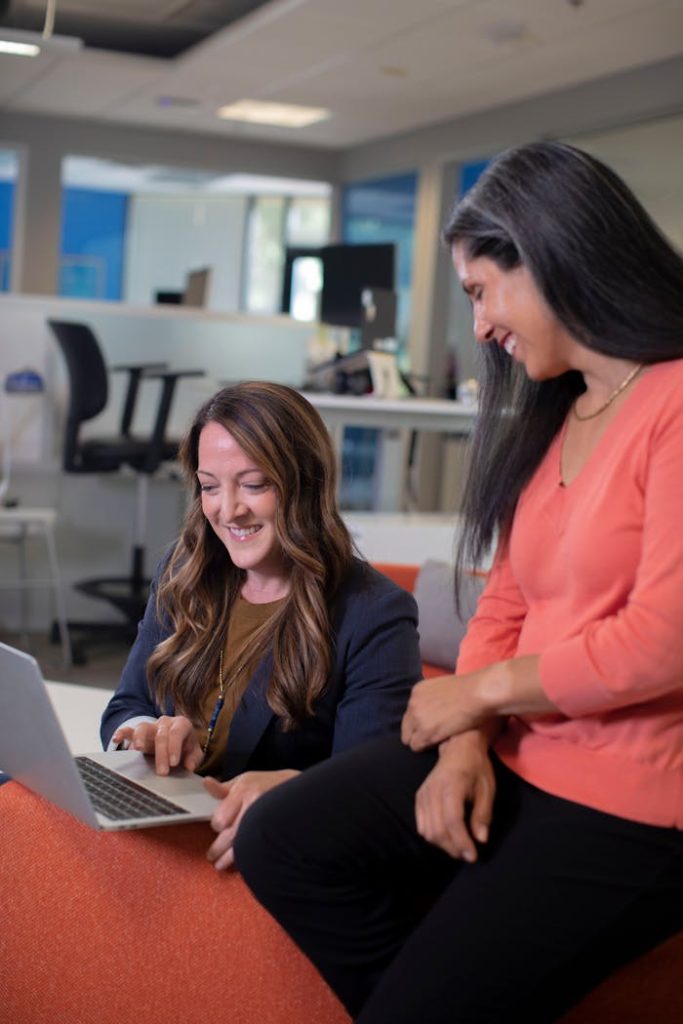 Two women working together on a laptop in a contemporary office setting.