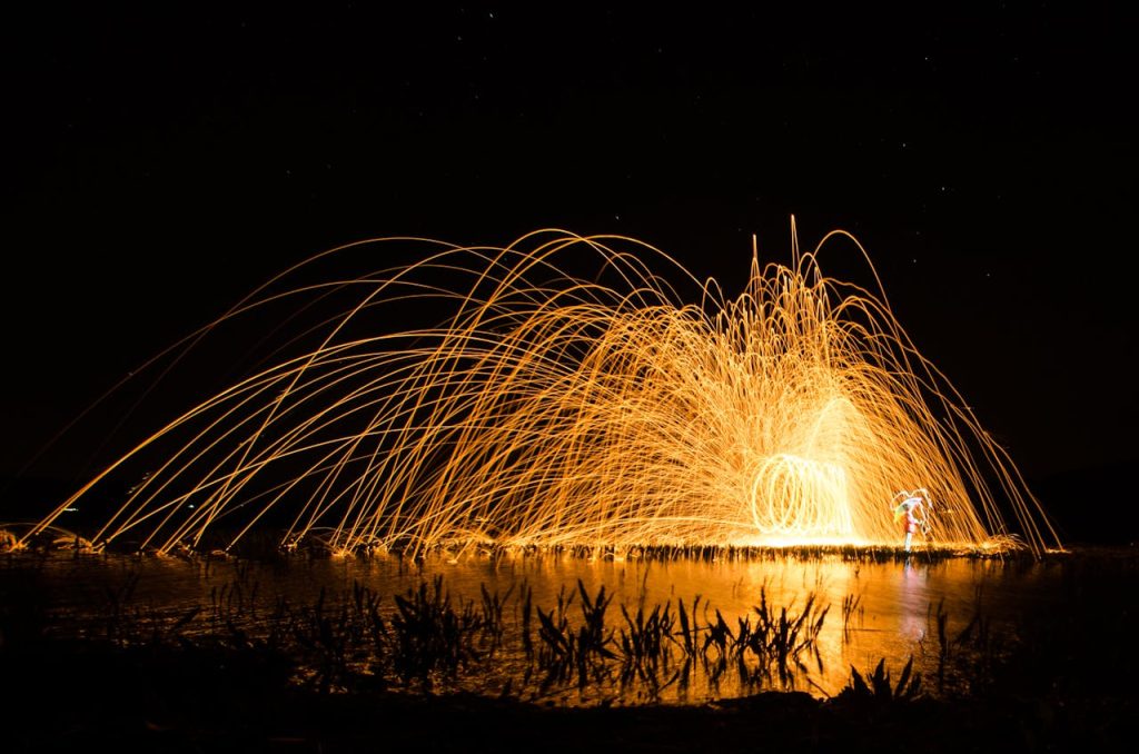 Captivating night photography of steel wool spinning with vibrant sparks reflected on water in Manisa, Türkiye.